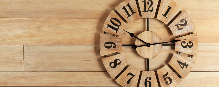 Wooden clock with large numbers on a light wood plank wall, symbolizing the durability of high quality LVP floors.