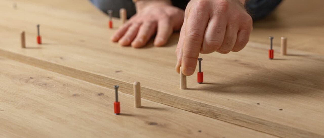Hands installing wooden pegs on flooring, illustrating challenges with DIY flooring projects without professional help.